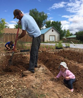 A gardener digging a bed at Ten Sleep Garden while a toddler in a sun hat plays in the soil